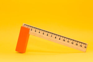 Photograph of a 15 cm wooden ruler resting on an orange support on a yellow background.