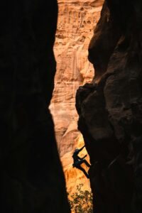 A photograph of a person climbing a canyon. The person is in the middle of the route, heading for the top.