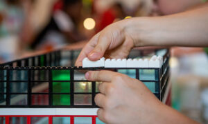 Fotografía en color que muestra las manos de un niño construyendo un edificio con Legos.