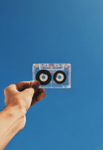 Fotografía de una mano sujetando una cinta de casete sobre fondo azul.