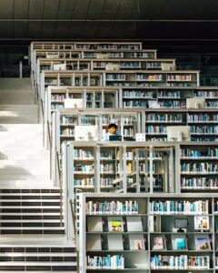 Fotografía de una persona estudiando entre las estanterías de una biblioteca. Fotografía de una persona estudiando entre las estanterías de una biblioteca.