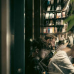 A photograph of researchers reading on laptops through the glass of a library, with books in the background.