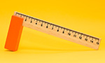 Fotografía de una regla de madera de 15 cm apoyada sobre un soporte naranja sobre fondo amarillo.