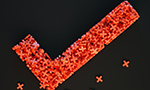 Fotografía de una marca de verificación formada por varias "X" de plástico rojo sobre un fondo negro.