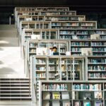 Fotografía de una persona estudiando entre las estanterías de una biblioteca.
