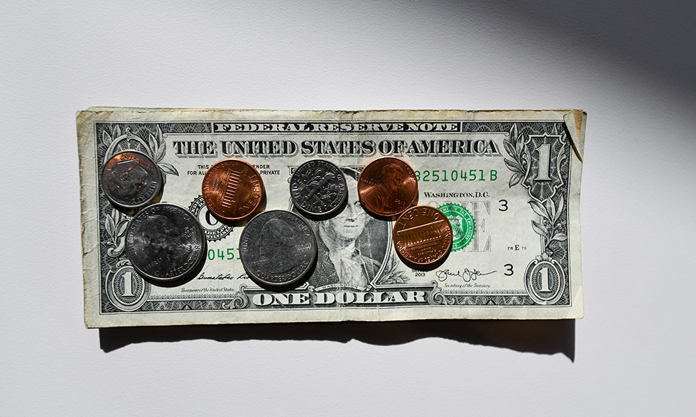 Fotografia de uma nota de um dólar em uma mesa branca com sete moedas sobre a nota.
